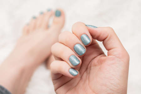 Female hand with silver nail design. Glitter silver nail polish manicure. Female hand and feet on white fluffy background.の写真素材