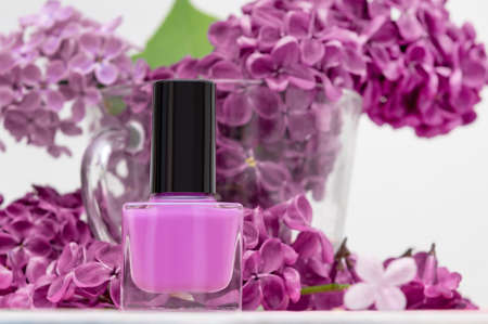 Pink nail polish bottle on purple lilac blossom background. Pink nail polish bottle on flower backgroundの写真素材