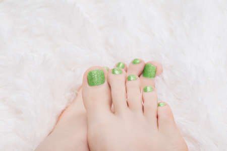 Female feet with green nail design. Glitter green nail polish pedicure on white fluffy backgroundの写真素材