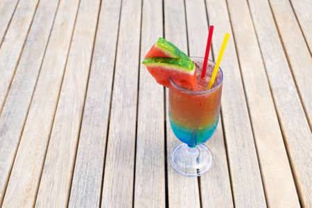 Rainbow cocktail on a wooden table. Concept of luxury vacation. Colorful mocktail at ocean beach barの写真素材