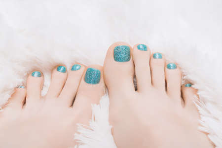 Female feet with marine nail design. Glitter cyan nail polish pedicure on white fluffy backgroundの写真素材