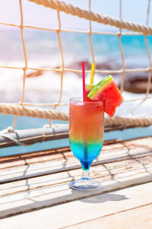 Rainbow cocktail on a wooden desk at seashore bar. luxury holidays. Colorful mocktail at ocean beach barの写真素材