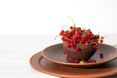 Brown bowl of red currant on white wooden desk. Ripe red current on two plates on white background. copy spaceの写真素材