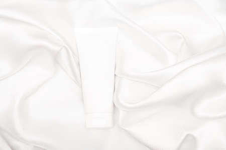 Unbranded white tube of cosmetic product on white background. Skin care lotion or cream on white fabric backgroundの写真素材