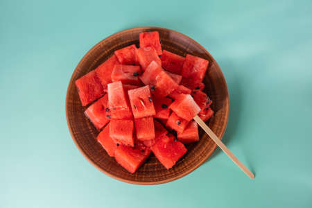 Ripe juicy red watermelon cubes in a brown clay plate on blue background. Watermelon cubes ready to eatの写真素材