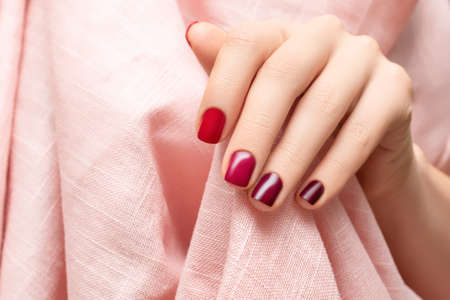 Female hand with dark red nail design. Glitter red nail polish manicure. woman hand hold pink fabric