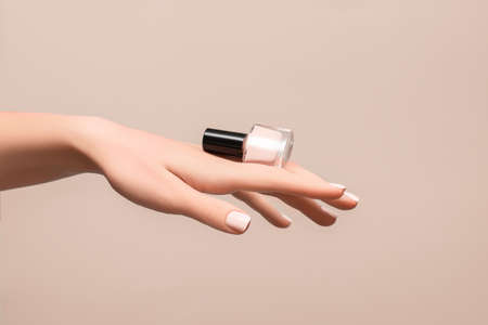 Female hand with pink nail design. Pink nail polish manicure. Woman hand hold pink nail polish bottleon beige background. copy space.の写真素材