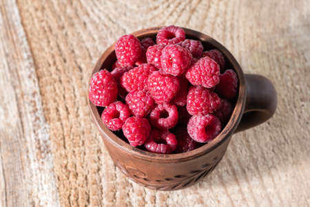 Fresh red raspberries in a brown cup on wooden desk. Ripe raw raspberries in a cup. Natural...