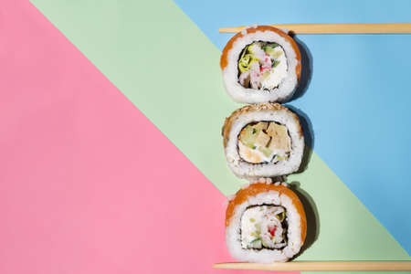 Fresh salmon sushi with wooden chopsticks on green, red, and blue background. Sushi rolls with chopsticks. fish sushi rollsの写真素材