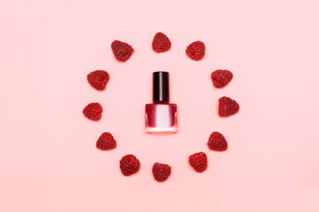 Red nail polish bottle in red raspberries circle on pink background. Red nail polish bottle on berries backgroundの写真素材