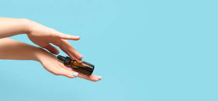 Woman hands with blue manicure. Female holding essential oil bottle on blue background. Female healthcare wellness concept. copy space.の写真素材