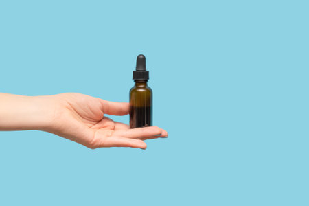 Woman hand with blue manicure. Female holding essential oil bottle on blue background. Female healthcare wellness concept. copy space.の写真素材