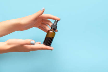 Woman hands with blue manicure. Female holding essential oil bottle on blue background. Female...