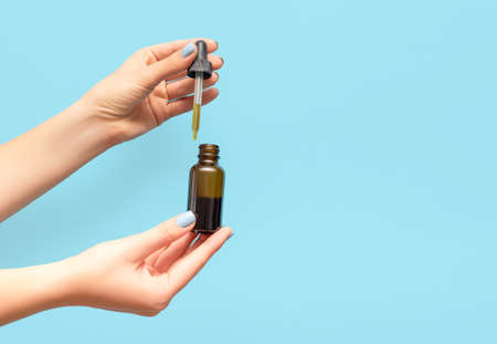 Woman hands with blue manicure. Female holding pipette and essential oil bottle on blue background. Female healthcare wellness concept. copy space.の写真素材