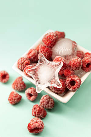 Frozen raspberries in white plate on blue background. Frozen ripe raspberries with ice stars and...