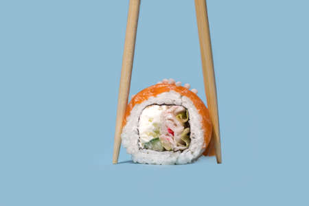 Fresh salmon sushi with wooden chopsticks on blue background. Sushi roll with chopsticks. fish sushi rollの写真素材