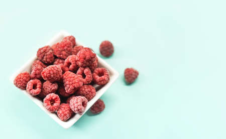 Frozen raspberries in white plate on blue background. Whole raw frozen berries. Frozen food concept. copy space.の写真素材
