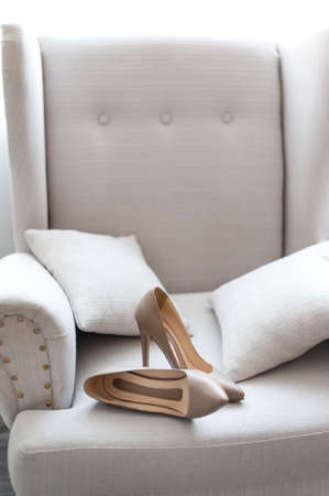 Beige wedding shoes on white chair close up. Luxury pair of high heel female shoes on a chair. Female elegant shoes fashion style.の写真素材