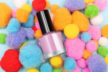Pink nail polish bottle on colorful soft pompom background. Pink nail polish bottle decorated with soft pompomsの写真素材