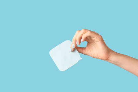 Female hand with blue manicure holding a white blank message card. Speech shape banner in female...