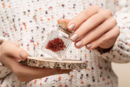 Female model hands with beige nail design. Glossy beige nail polish manicure. Woman hands hold bottle with saffron spiceの写真素材