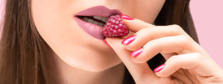 Perfect pink female lips. Close up of pink female lips with raspberry. Beautiful female model lips eating raspberry. Pink lips with raspberries. Female hand with glitter red nail design.の写真素材