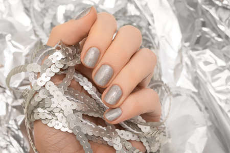 Female hand with glitter silver nail design. Female hand hold shiny metal sequins. Female model hand on glitter silver background. Glitter silver nail polish manicure.の写真素材