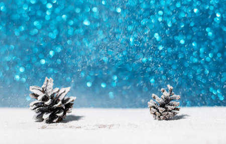 Winter background with pine cones. Winter Christmas background with two fir cones, glitter blue snowstorm and place for product or text in the middleの写真素材