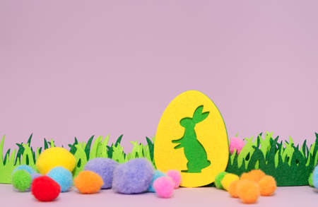 Easter post card with Easter bunny, green fabric grass and colorful fluffy balls on purple...