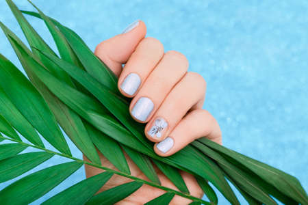 Female hand with light blue nail design. Glitter blue nail polish manicure with fantastic flower...