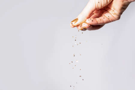 Small gold star shape sequins fall from young female hand on gray background. Happy New Year celebration concept. Female pour gold star shape sequins on gray background.の写真素材
