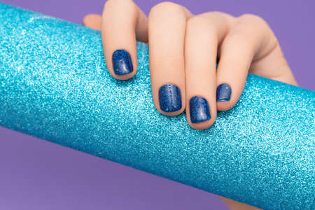 Female hand with blue nail design. Glitter blue nail polish manicure. Woman hand hold glitter blue...