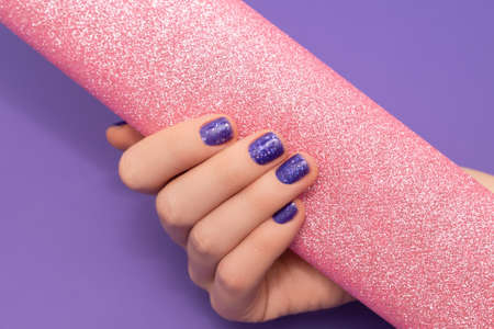 Female hand with purple nail design. Glitter purple nail polish manicure. Woman hand hold glitter...