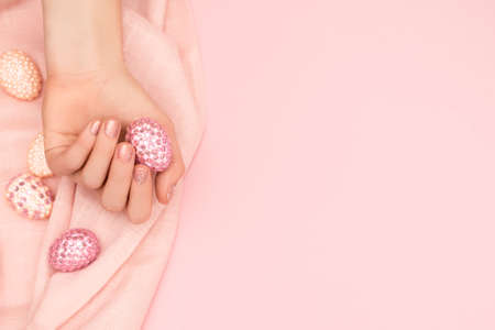 Female hand with glitter pink nail design. Female hand hold easter egg decorated with pink gems. Model hand with spring nail design on pink background. copy space.の写真素材