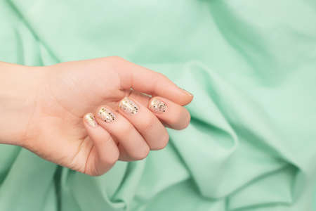Female hand with clear nail design. Glitter clear nail polish manicure with green nail art. Woman hand hold light green fabric on green backgroundの写真素材