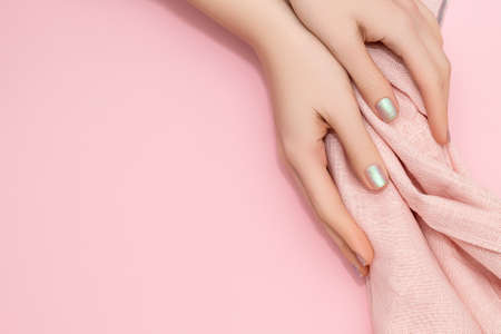 Female hands with glitter pearlescent nail design. Glitter pearlescent nail polish manicure. Female model hands with pink fabric on pink background. copy spaceの写真素材
