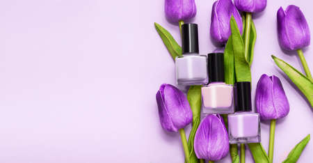 Three purple nail polish bottles with fresh spring tulip flowers on a pink background. Spring...