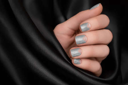 Female hand with silver nail design. Glitter silver nail polish manicure. Female model hand with perfect manicure on black fabric backgroundの写真素材