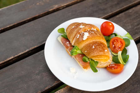 Fresh croissant with smoked salmon and cheese. Tasty fish croissant with red ripe cherry tomatoes on...