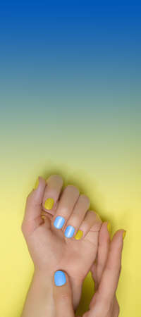 Female hands with ukrainian nail design. Glitter yellow and blue nail polish manicure. Female hands on blue and yellow background. Copy space Copy space.の写真素材