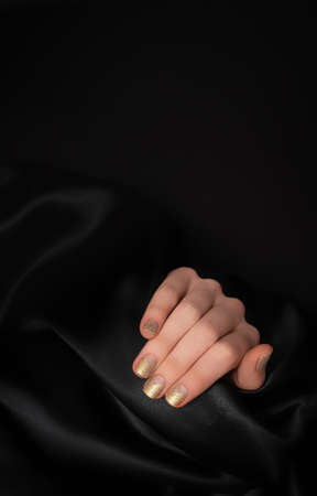 Female hand with golden nail design. Glitter gold nail polish manicure. Female model hand with perfect manicure on black fabric background. Copy space.の写真素材