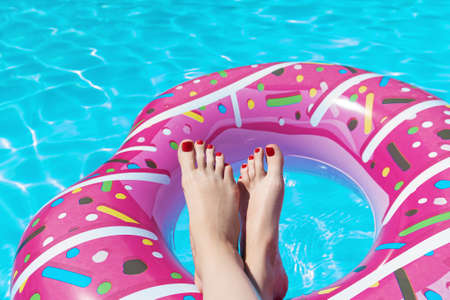 Female with perfect red pedicure over a pool with water splash. Vacation pericure. Female with bare feet on rubber ring over blue swimming pool waterの写真素材