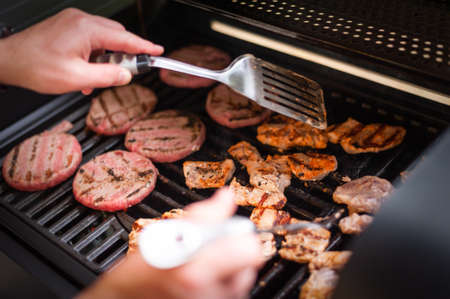 Cooking burger on outdoor gas grill. Beef cutlets cooked on a gas grill outdoor. Male check cutlets...