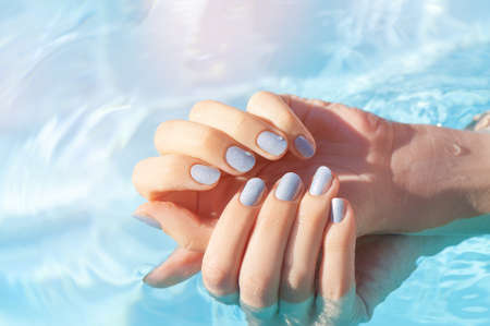 Female hands with vacation nail design. Glitter blue nail polish manicure. Female hands on a blue pool background.の写真素材