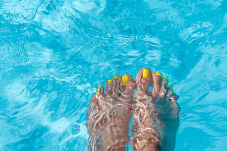 Female with perfect yellow pedicure over a pool with water splash. Vacation pericure. Female bare...