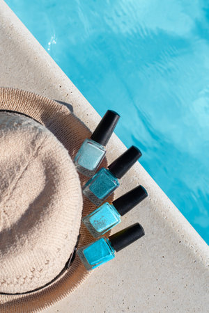 Blue nail polish bottles with hat on a pools edge. Nail polish bottles near blue pool water. Vacation manicure nail polish concept. Summer nail polish set with copy space. High quality photo.の写真素材