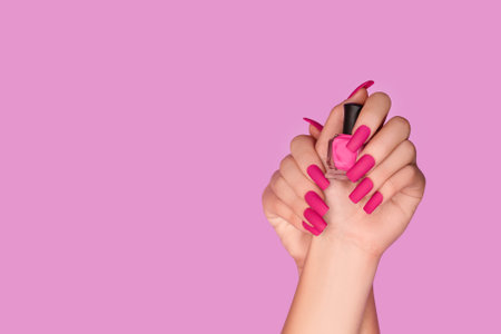 Female hands with pink nail design. Mate pink nail polish manicure. Female model hands with perfect manicure hold pink nail polish bottle on pink background. Copy space. Place for text.の写真素材