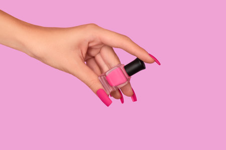 Female hand with pink nail design. Mate pink nail polish manicure. Female model hand with perfect manicure hold pink nail polish bottle on pink background. Copy space. Place for text.の写真素材