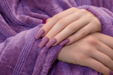 Female hands with purple nail design. Mate purple nail polish manicure. Female model hands with perfect manicure hold purple fluffy fabricの写真素材