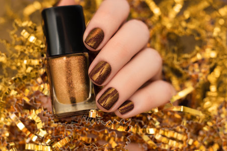 Female hand with Christmas nail design. Glitter chocolate nail polish manicure. Female model hand with perfect brown manicure hold brown nail polish bottle on golden Christmas decorationsの写真素材